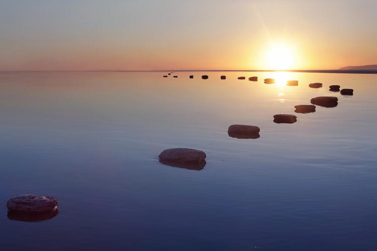 a body of water with rocks in it and the sun setting